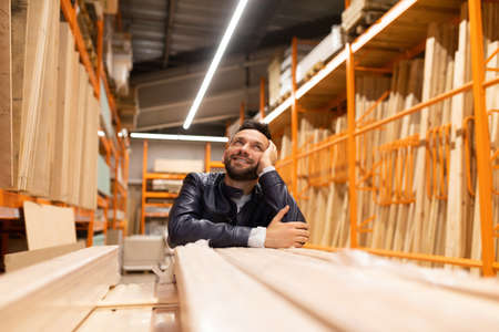 happy customer in a hardware store looks at racks with planks and wooden blocks, with plywood and chipboard and OSB sheetsの写真素材