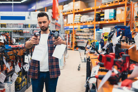 a male customer in a hardware store in the power tool department compares two screwdriversの写真素材