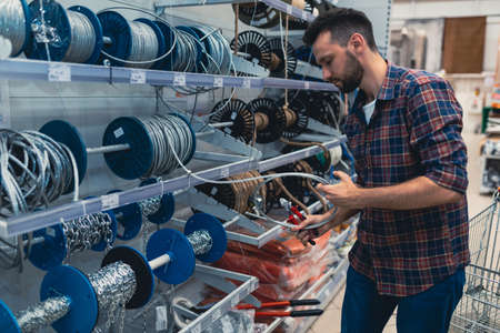 a man in a hardware store buys a safety metal cable for high-altitude work.