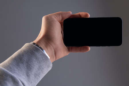 black rectangular modern smartphone in a male hand on a gray isolated background horizontally, phone...