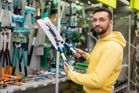 a man before the start of a new gardening season chooses large scissors a pruner for trimming bushes and tree branchesの写真素材