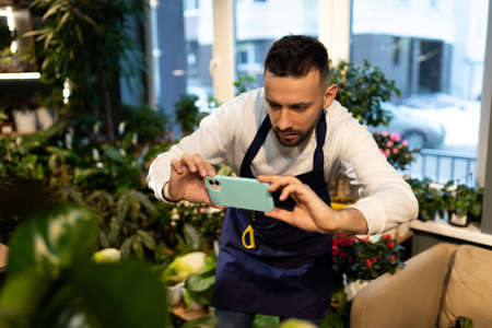 businessman botanist in the garden center photographing flowers on a smartphone