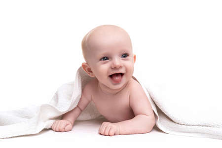A cheerful newborn laughs on a white background peeking out from under a towel