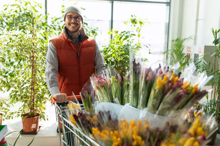 an employee of a store for garden plants and flowers carries a cart with bouquets of tulips