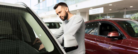 a man carefully examines new cars in a car dealership