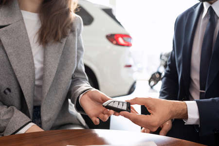 the seller in the car dealership gives the key to the new car to the buyerの写真素材