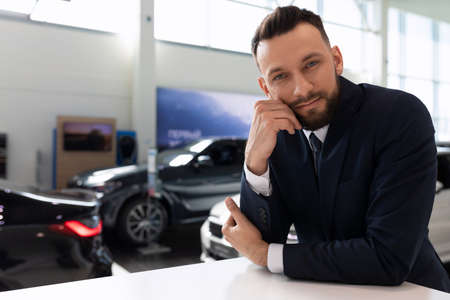 portrait of an employee of a car dealership in the showroom against the background of new carsの写真素材