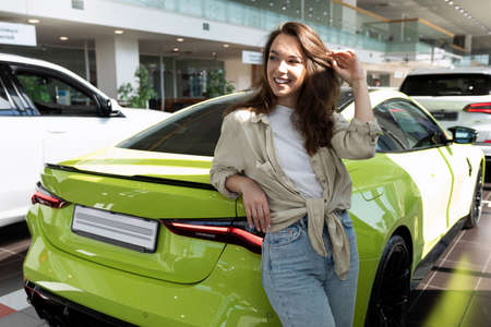 young beautiful woman next to a sports car in a car dealership