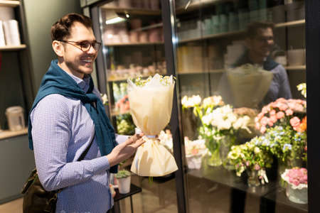 satisfied client of flower salons with a bouquet in his hands next to the refrigerator