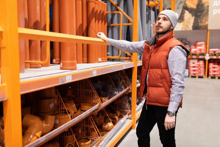 a man chooses sewer plumbing pipes in a hardware hardware storeの写真素材