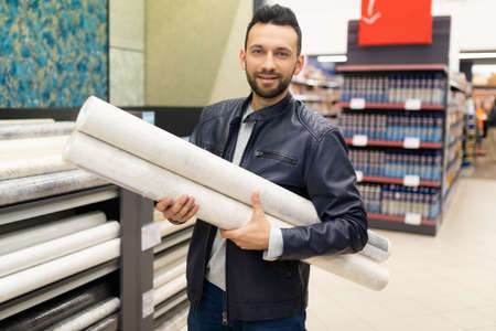 pretty shopper holding an armful of rolls of paper wallpaper in a hardware storeの写真素材