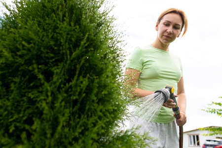 young woman gardener takes care of the lawn by watering it with water from a hoseの写真素材