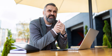 portrait of serious businessman with laptop in city cafe working onlineの写真素材