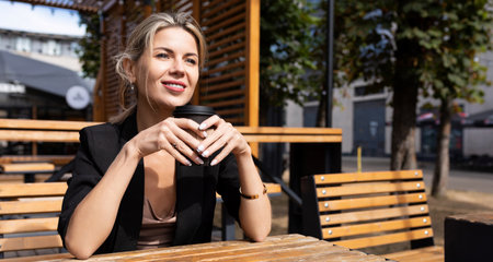 confident business woman drinking coffee in a street cafe with a smile on her faceの写真素材
