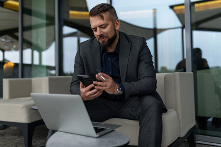 a man in a business suit works in a street cafe on a laptop with a mobile phone in his hands and smokes a cigaretteの写真素材