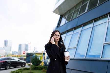 Business woman rushing to a meeting talking on a mobile phone with a cup of coffee in her handsの写真素材