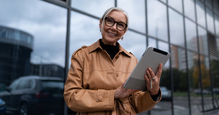 elderly stylish woman with a tablet on the background of a business center, woman leader in business...