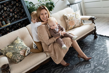 happy mom fooling around with two boys sons sitting on sofa