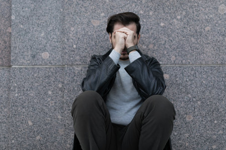 grieving man sitting upset covering his face with his handsの写真素材