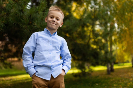 portrait of a cheerful boy in a blue shirt standing with his hands in his pockets against the backdrop of an autumn forestの写真素材