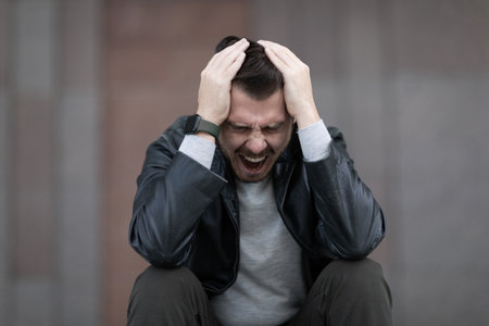 a man with a migraine attack sits clutching his head and screamingの写真素材