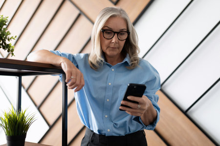 Business successful woman 50 years old looking at the screen of a mobile phone in the office. Financial Business Analytics Data Dashboard conceptの写真素材