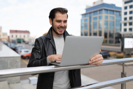 young caucasian man with a smile on his face works on laptops outsideの写真素材