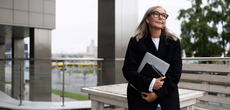Business woman on the terrace of an office building with a laptop in her hands, caucasian Middle aged older businesswoman at work Conceptの写真素材