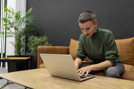 Strong woman with short haircut working on laptop while sitting on sofa at homeの写真素材