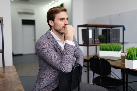 a business man in a jacket sits on a chair in the office, thinking, looks aheadの写真素材