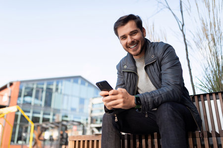 young man in jacket with phone outside