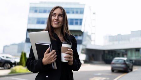 adult successful caucasian female boss with a laptop and a notebook in her hands looks at the camera...