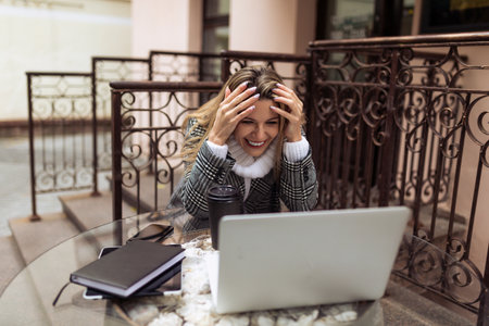a young girl freelancer sits at a table in a cafe on the street with a laptopの写真素材