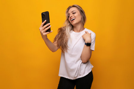 a girl with a phone in her hands takes a photo on a yellow backgroundの写真素材