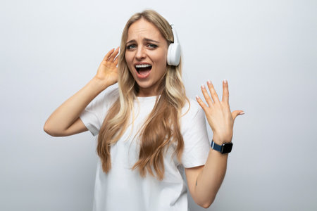 young woman sings along to music from headphones among white backgroundの写真素材