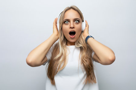 surprised girl with a grimace in white headphones listens to loud music on a white background