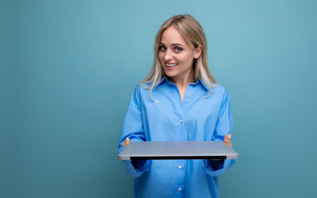 smiling cheerful blond girl student with a laptop computer on a bright blue backgroundの写真素材