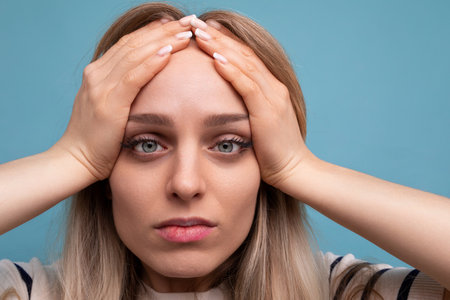 close-up of an upset girl in casual clothes holding her head on a blue isolated background