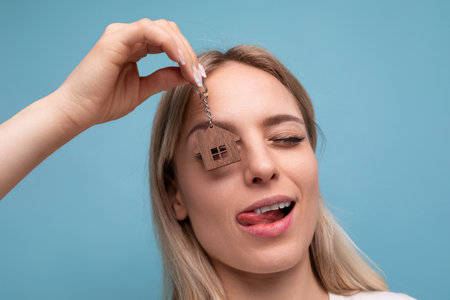 close-up photo of a joyful happy young woman holding a keychain of her new property on a blue isolated backgroundの写真素材