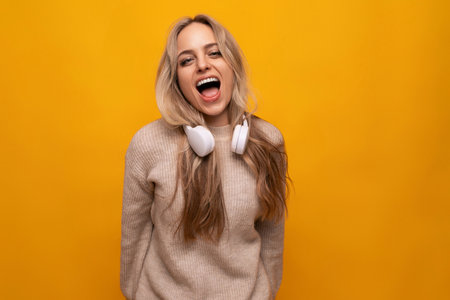 girl with a grimace in headphones on a yellow backgroundの写真素材