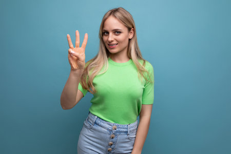 bright smiling girl in casual outfit shows three fingers on a blue backgroundの写真素材