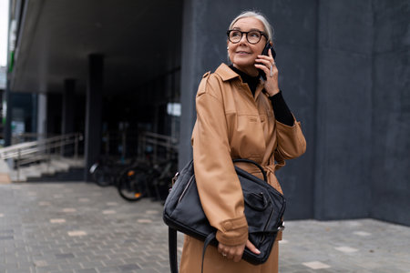 photo of a mature adult female economist with gray hair during a break with a phone in her hands against the backdrop of a business centerの写真素材