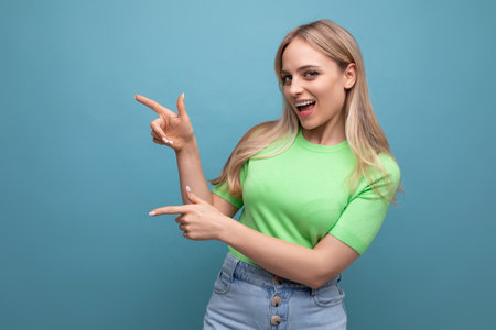 energetic girl in casual outfit pointing at the wall on the left on a blue backgroundの写真素材