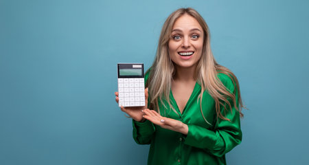european pleasantly perplexed stylish blonde girl with a calculator on a blue backgroundの写真素材