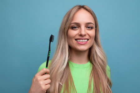 young blond woman with healthy teeth holding a toothbrush on a blue backgroundの写真素材