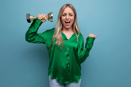 adorable girl squeals with joy holding the championship cup on a blue bright backgroundの写真素材