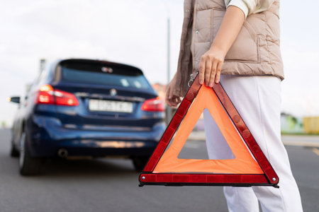 a woman driver puts a triangular road sign due to a car breakdown on the roadの写真素材