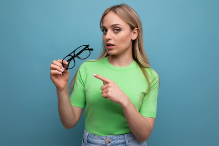 young female consultant demonstrates glasses in a black frame for vision on a blue backgroundの写真素材