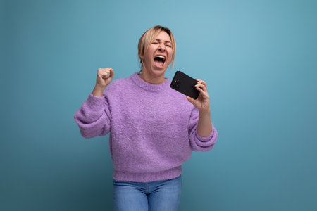 energetic blond young woman consultant in purple hoodie holding smartphone with mockup and singing...