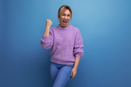 cheerful energetic blond young woman consultant in purple hoodie rejoices on blue background with copy spaceの写真素材
